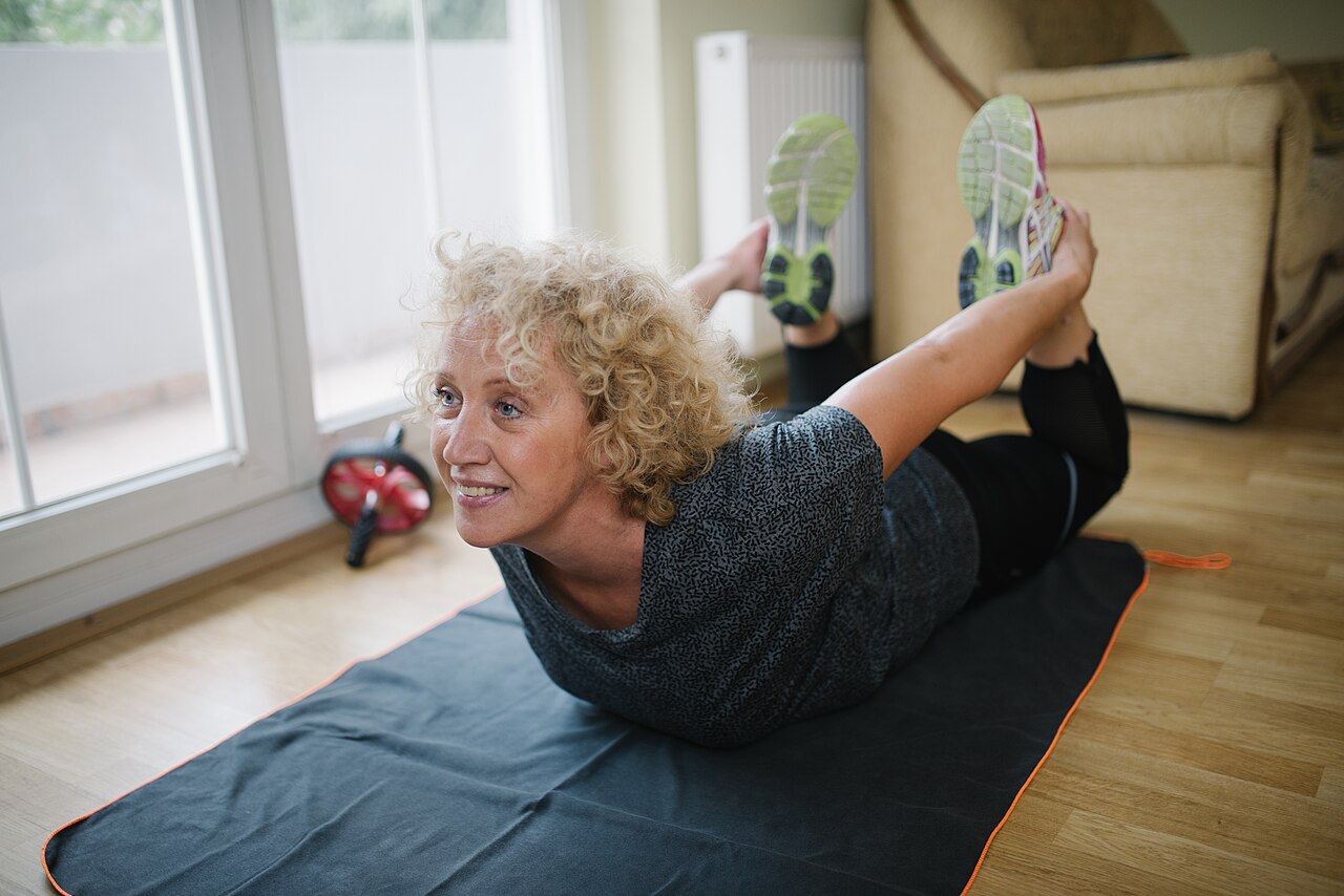 A person lying face down in Bow Pose, holding the ankles with the chest and thighs lifted