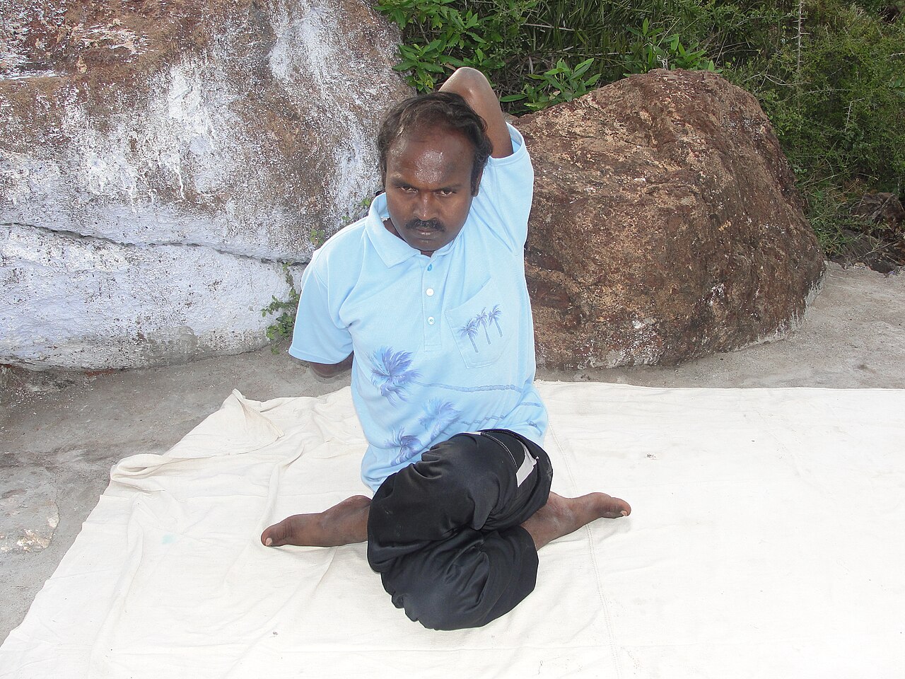 A person seated in Cow Face Pose with knees stacked and one arm reaching down the back