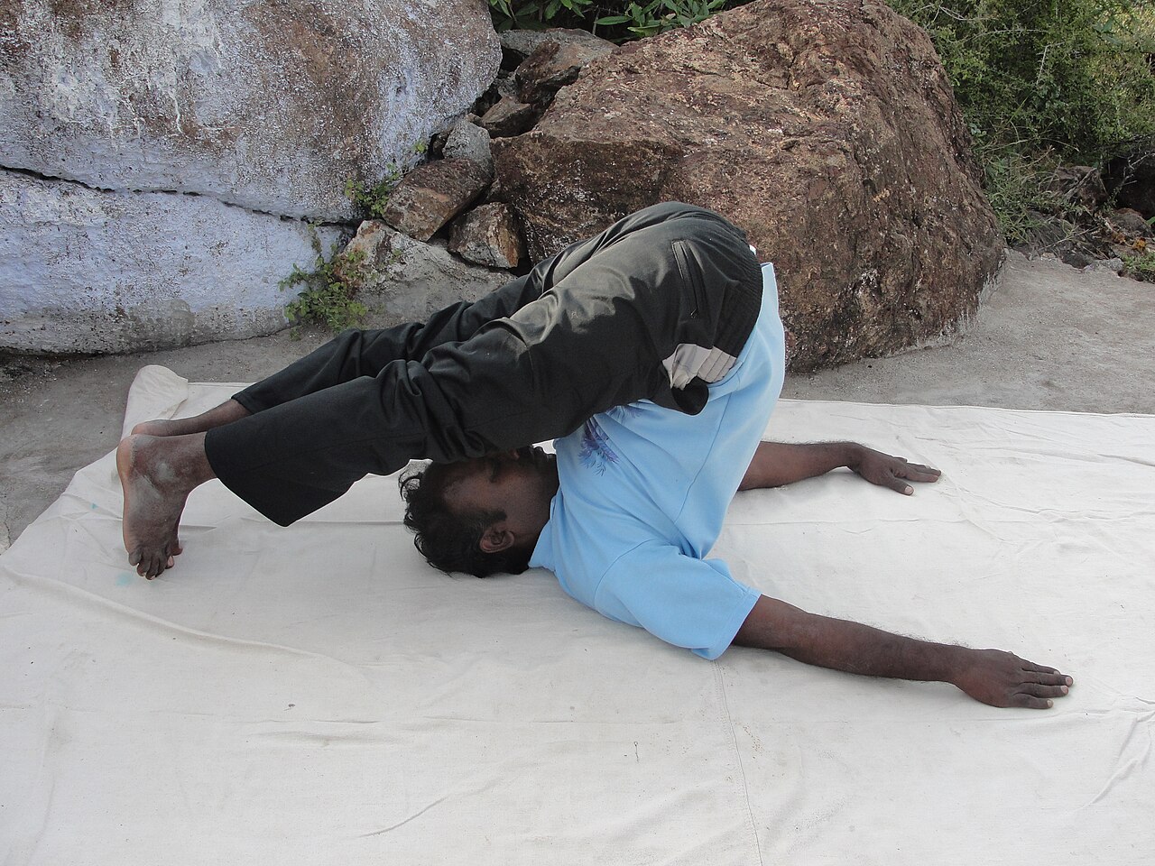 A person in Plow Pose with legs folded over the head and toes reaching the floor
