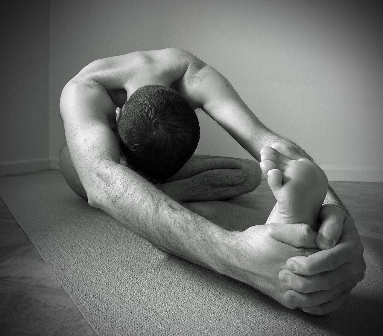 A person seated in Head-to-Knee Pose, folded over one extended leg