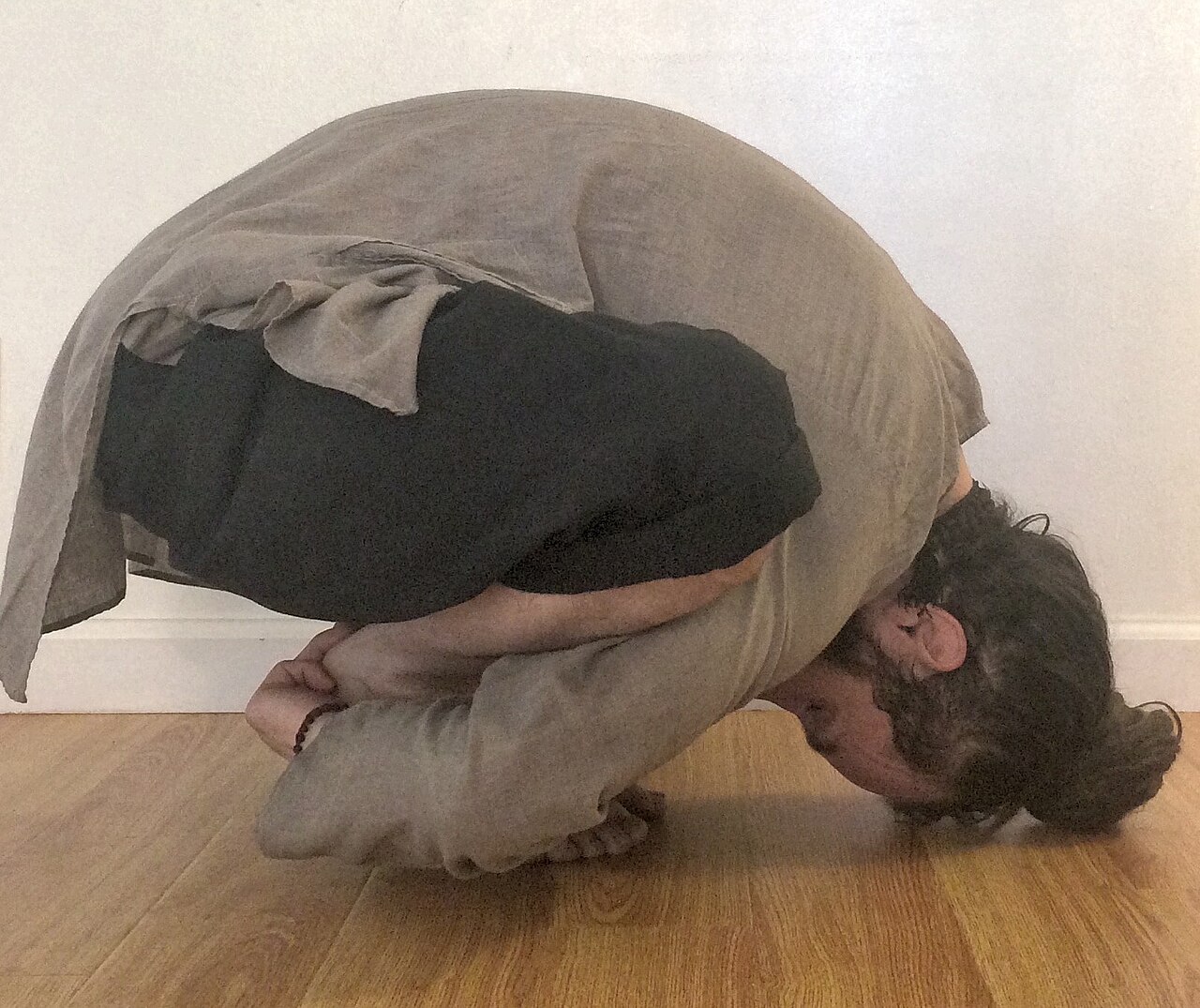 A person in a deep squat in Garland Pose, holding the heels with the torso folded forward