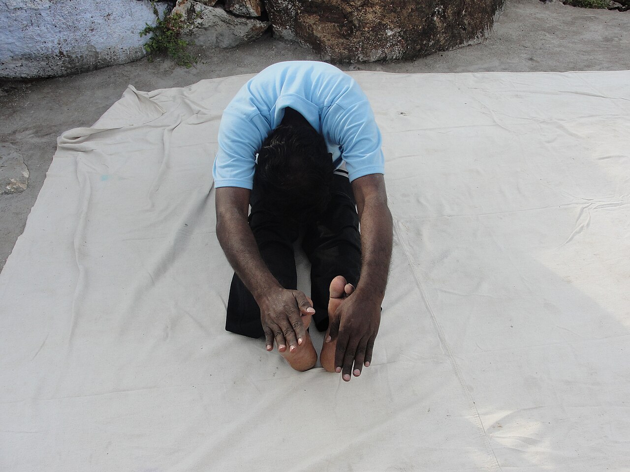 A person seated in a forward fold, reaching toward the feet with a long spine