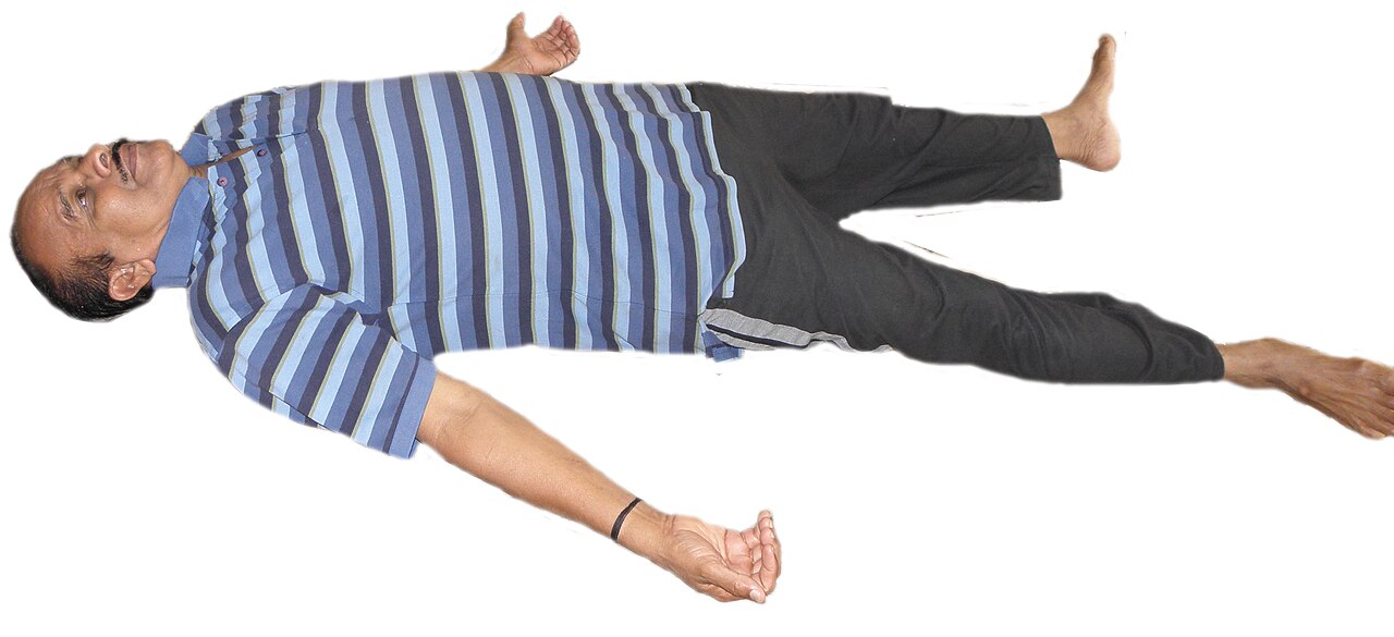 A person lying flat in Corpse Pose with arms and legs relaxed