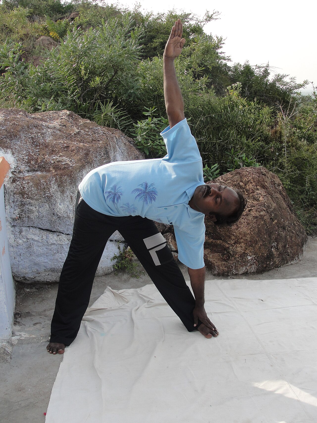 A person in Triangle Pose with legs wide, one hand on the shin and the other arm reaching up