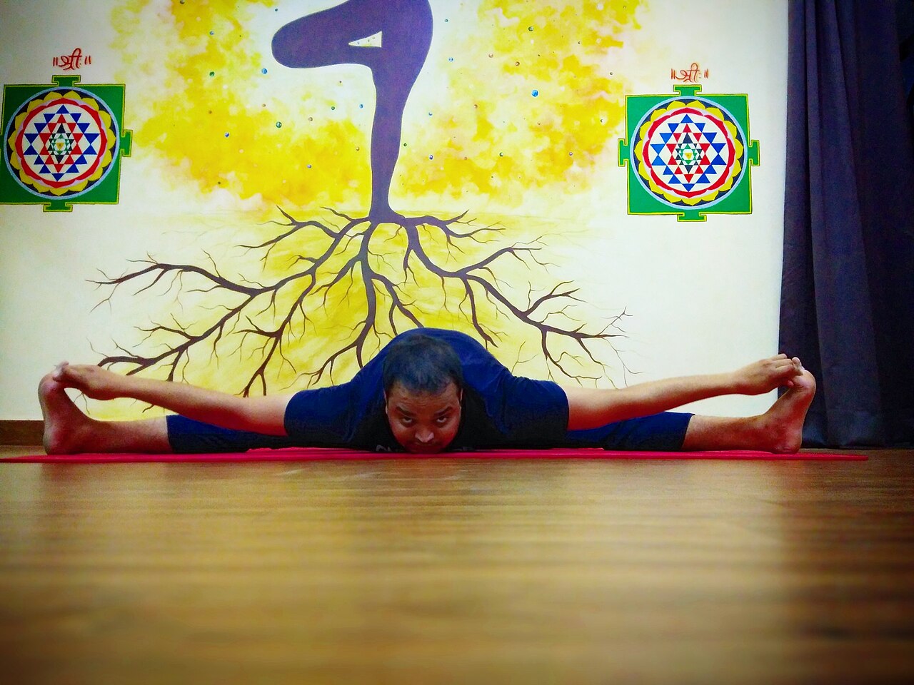 A person seated in a wide-legged forward fold, reaching between the legs